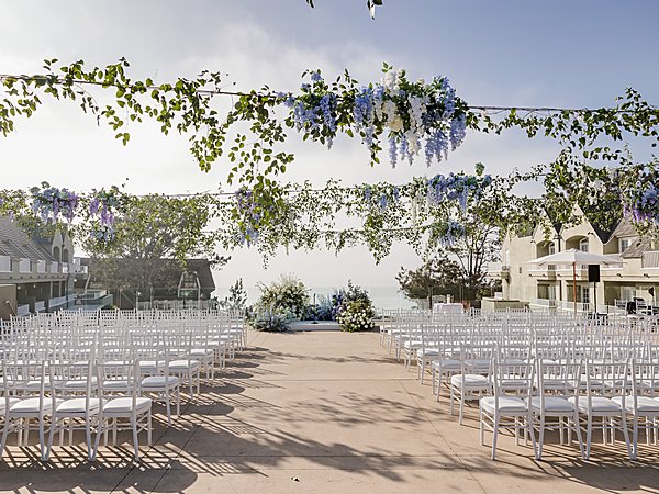Ocean-view wedding ceremony setup with white chairs and hanging wisteria florals at L'Auberge Del Mar resort in Del Mar, California